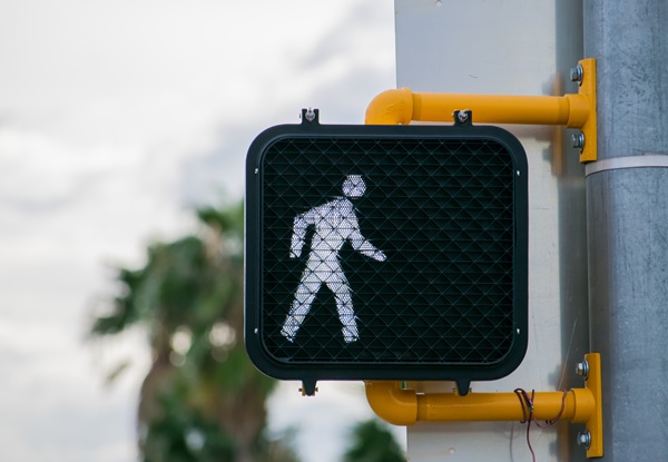 Illuminated pedestrian walk signal at a crosswalk, indicating it is safe for people to cross the street.
