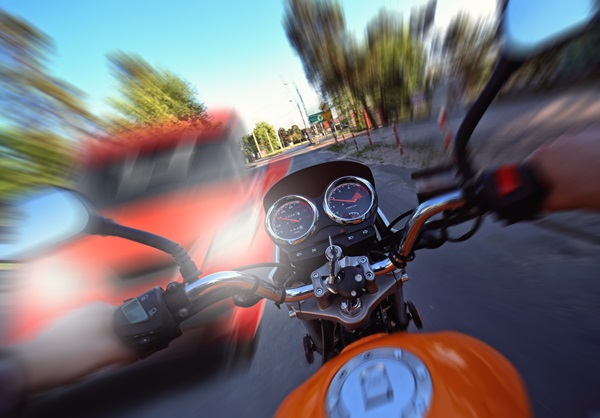 First-person view from a motorcyclist approaching a red vehicle at high speed, with motion blur indicating an imminent collision.
